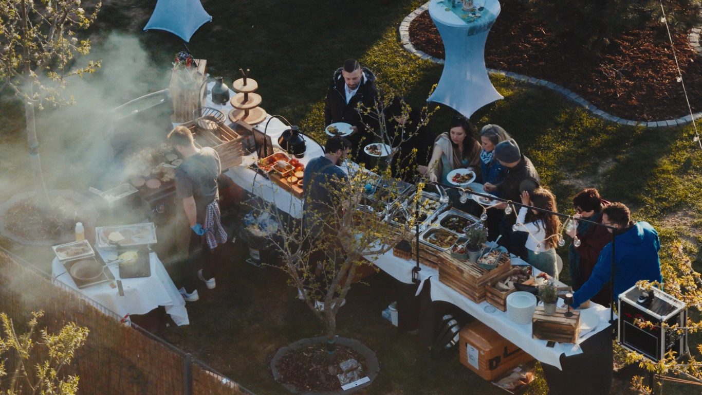 Zwei Köche von CulinART arbeiten am Grill, im Hintergrund Gäste mit Tellern bei einer Gartenfeier